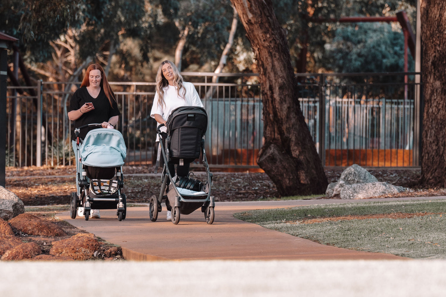 Mothers walking in park setting with babies napping in pram