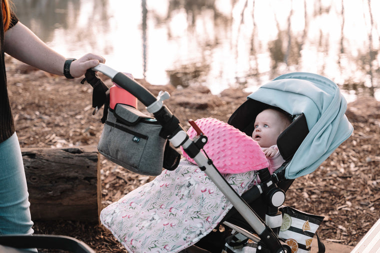 Baby in a stroller with a pink cover and floral pattern, outdoors.